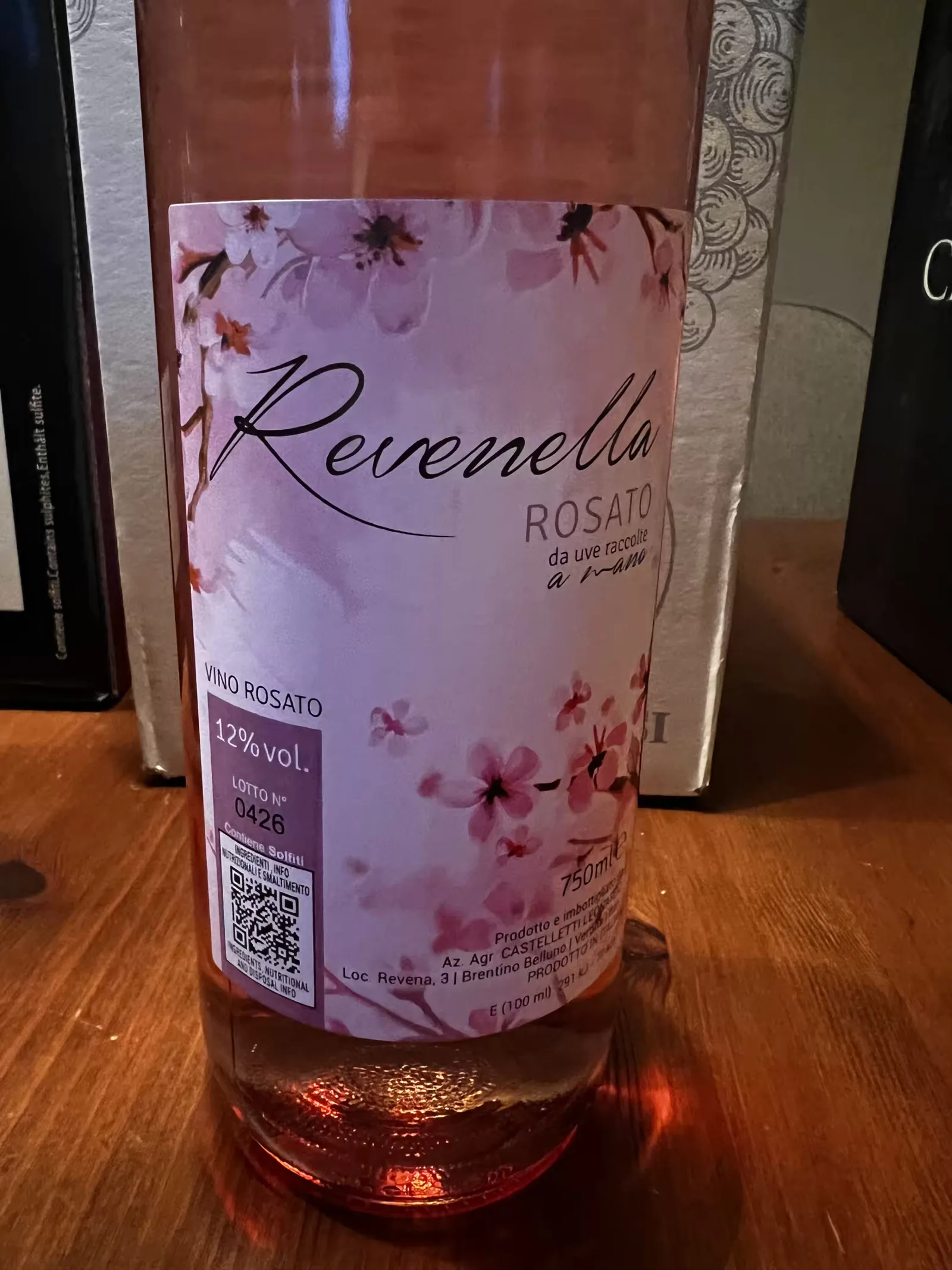 Bottiglia di Revenella Rosato con etichetta rosa su pavimento in legno.