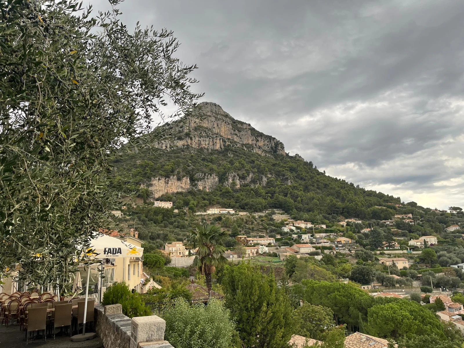 Blick auf Saint-Jeannet und einen bewaldeten Felsberg unter grauen Wolken.