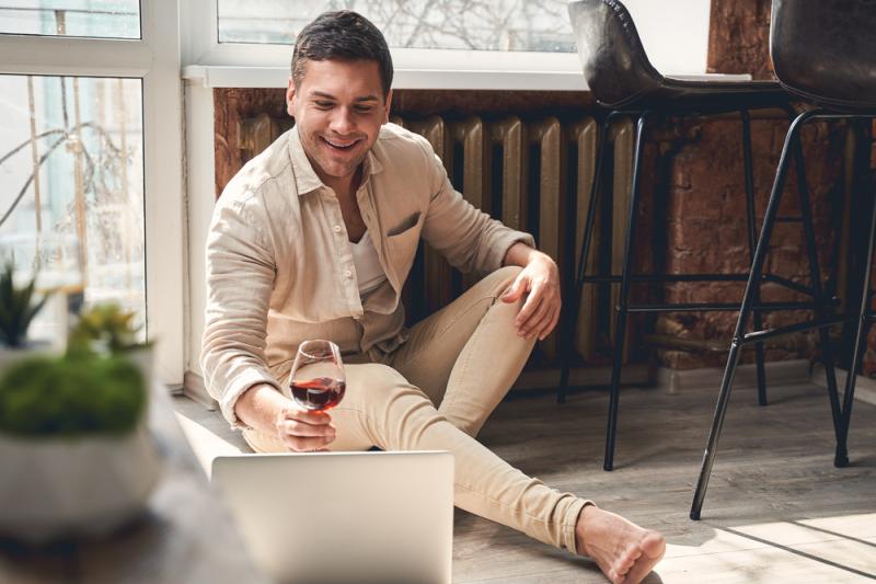 Un hombre con vino delante del portátil